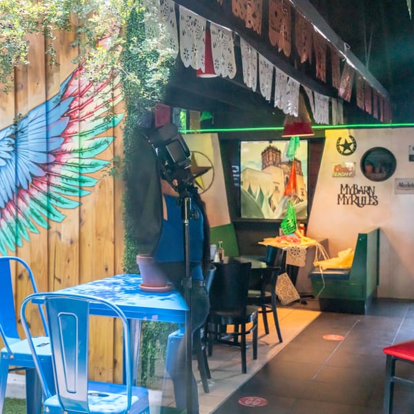 A vibrant restaurant interior with a colorful wing mural, blue tables, and Mexican-themed decor.