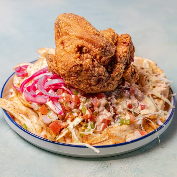 Crispy fried chicken on a bed of plantain fries, topped with salsa, pickled onions, and sauce.