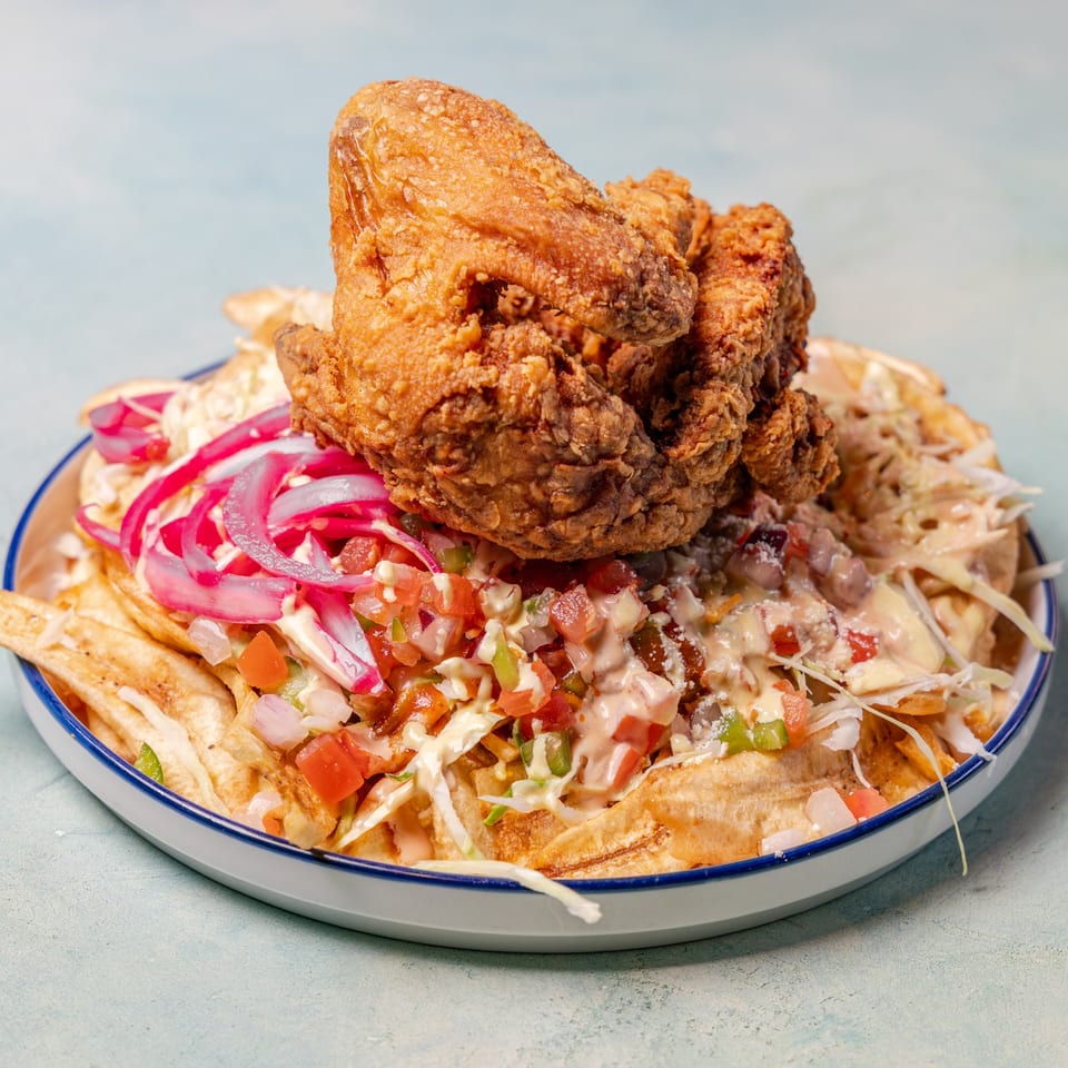 Crispy fried chicken on a bed of plantain fries, topped with salsa, pickled onions, and sauce.