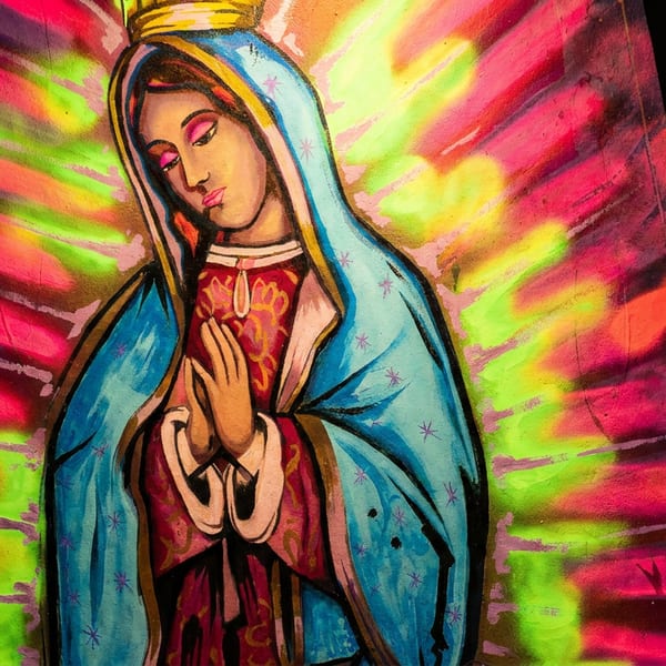 Colorful Virgin Mary mural with a bright neon pink and green background, inside a restaurant.