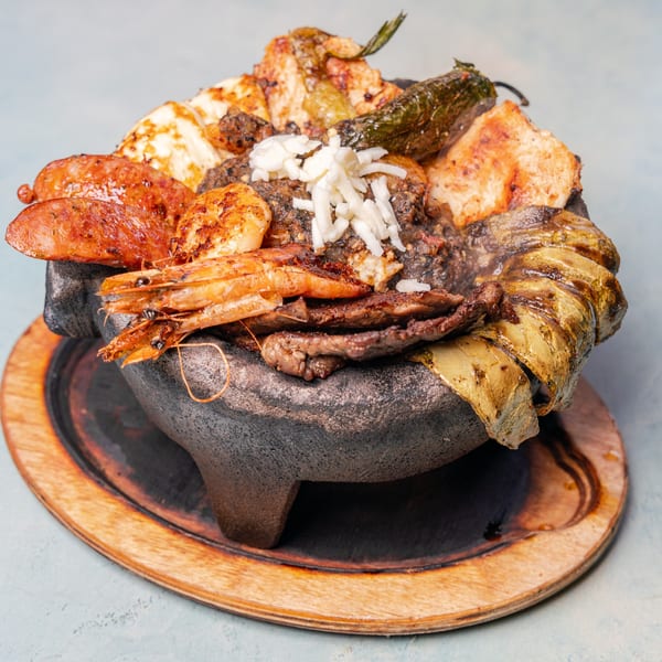 Sizzling stone platter piled with grilled shrimp, steak, sausage, cheese, vegetables, rice, and roasted green peppers.