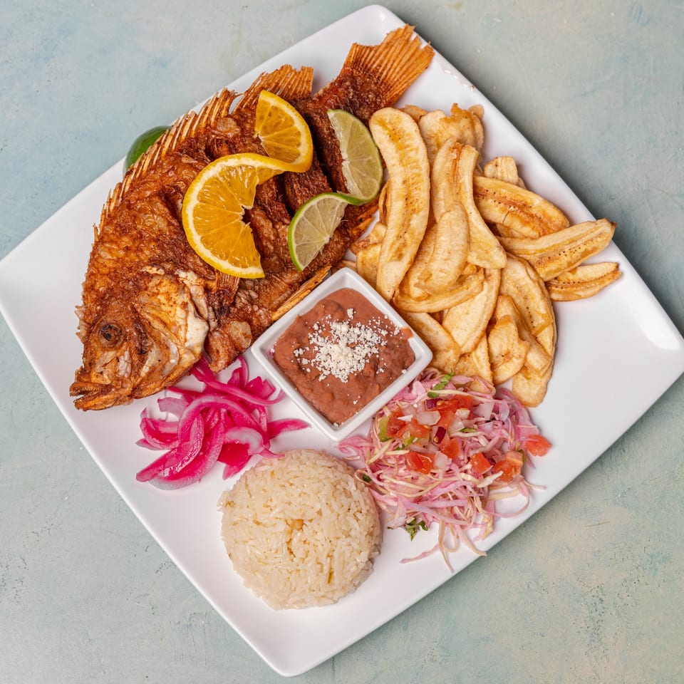 Whole fried fish with lemon and lime, plantain chips, rice, beans, pickled onions, and salad.