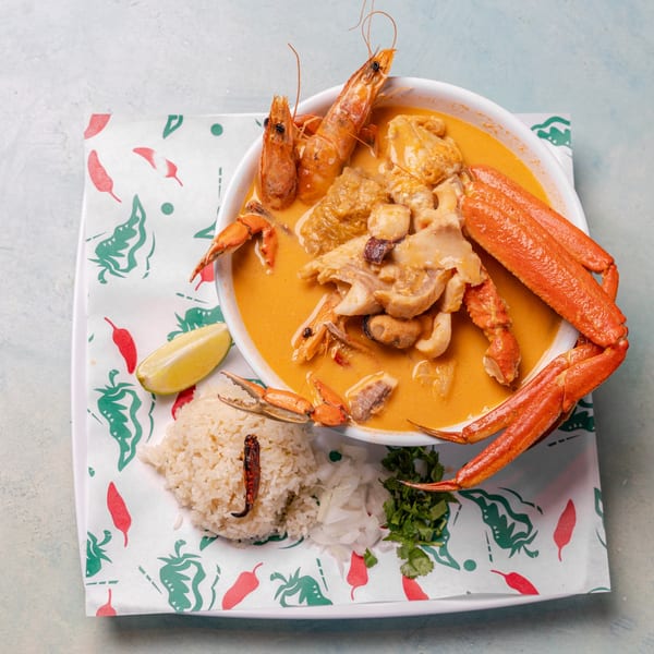 Seafood soup with crab legs, shrimp, and other seafood, served with rice, lime, and cilantro.