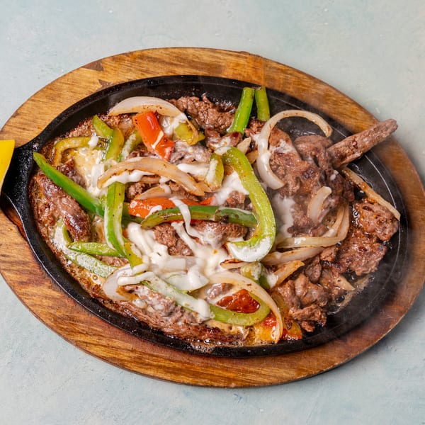 Sizzling beef fajitas with melted cheese, green and red peppers, and onions on a wooden platter.