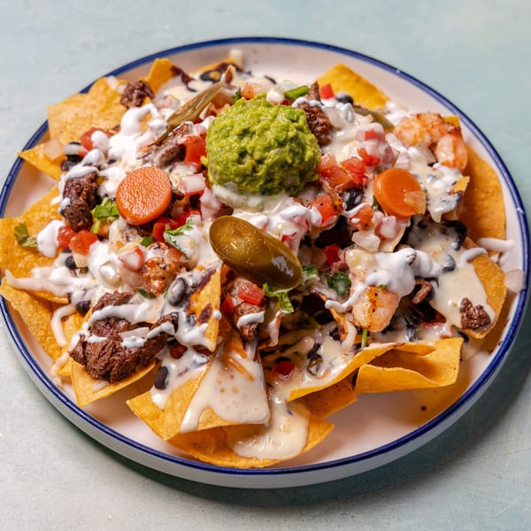 Loaded nachos topped with guacamole, grilled steak, shrimp, black beans, salsa, jalapeños, and creamy cheese sauce.