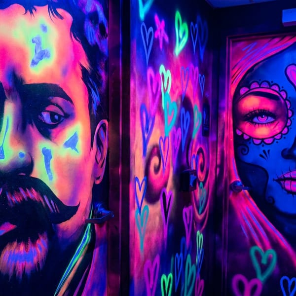 Blacklight murals of a man with a mustache and a woman with sugar skull makeup, surrounded by glowing hearts.