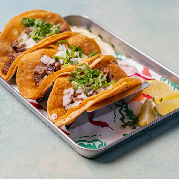 Tray of crispy beef tacos topped with diced onions and cilantro, served with lime wedges.