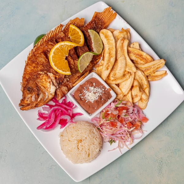 Fried whole fish with lemon and lime slices, plantain chips, rice, beans, and salad.