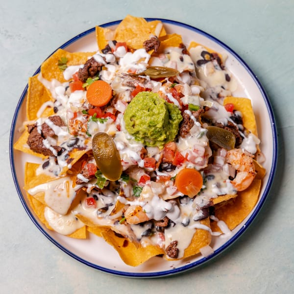A plate of loaded nachos with beef, shrimp, black beans, cheese sauce, guacamole, and jalapeños.